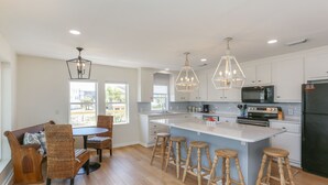 Una cocina moderna con una isla grande, taburetes de bar, una mesa de comedor con sillas e iluminación colgante.