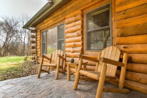 A log cabin with a stone-paved porch, wooden Adirondack chairs, and a window with blinds. - Cabin by the River: Visited by Treehouse Masters! (Ferryville)