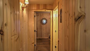 A wooden interior hallway with a staircase leading to a door with a circular window. - Cabin by the River: Visited by Treehouse Masters! (Ferryville)