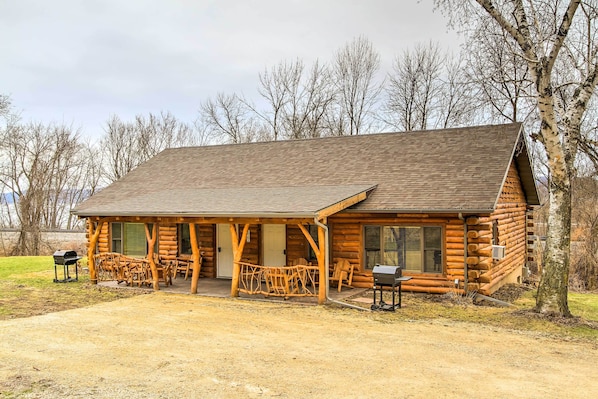 A log cabin with a porch, outdoor seating, and a grill area.