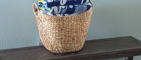 A woven basket with a blue and white patterned fabric inside, placed on a wooden bench against a light blue wall.