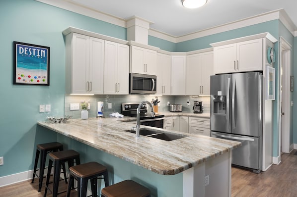 A modern kitchen with white cabinets, a stainless steel refrigerator, and a marble countertop.