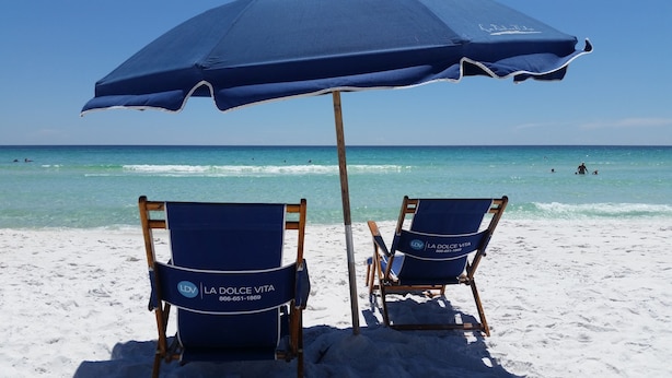 Deux chaises de plage avec un parasol bleu, sur une plage de sable.