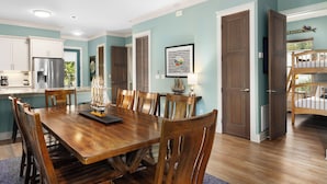 Un grand espace de salle à manger avec une table et des chaises en bois, une cuisine avec des meubles blancs et un mur d’accent de couleur turquoise.