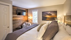 Ein Schlafzimmer mit einem Bett, einem an einer Holzwand montierten Fernseher, einem Fenster mit Jalousien und einem Gemälde an der Wand.