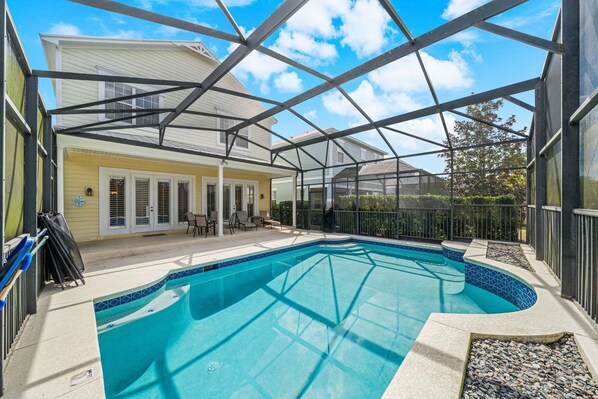 Una piscina con cerramiento de vidrio, un patio cubierto y una casa al fondo.