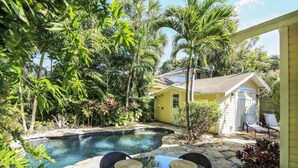 Ein Garten mit Schwimmbecken, umgeben von üppiger Vegetation und einem gelben Haus.