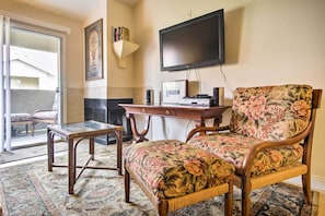 A living room with a glass-top table, a floral armchair, a wooden coffee table, a flat-screen TV, and a fireplace. - Pet-Friendly Las Vegas Condo: 1 Mi to the Strip! (Las Vegas)