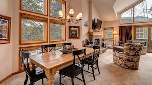 Un comedor amplio con una mesa y sillas de madera, una chimenea y ventanas grandes que dan a vistas de árboles.