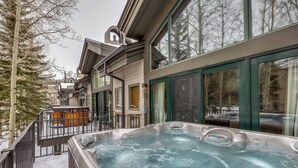 Un jacuzzi en un balcón con vistas a un paisaje nevado y un edificio con grandes ventanales.