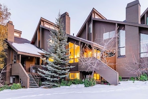 A modern multi-story building with a wooden exterior, large windows, and a staircase leading to the entrance.