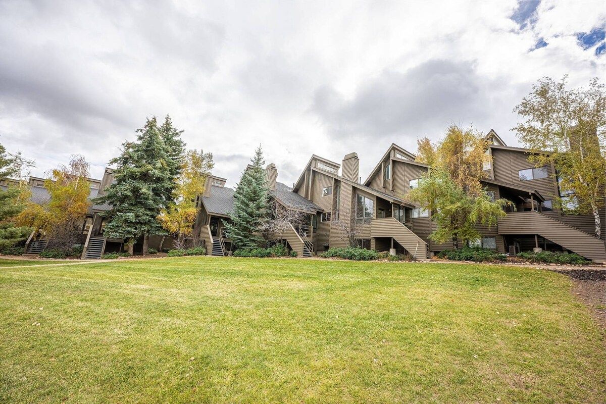 A residential building with multiple levels, a grassy front yard, and trees with autumn foliage.