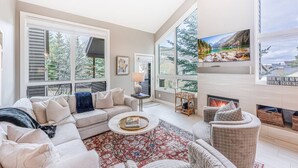 A spacious living room with a fireplace, large windows, and a cozy seating area. - Canyons Resort Ski Home | Walk to Skiing + Free On Call Shuttle | 2 Fireplaces & 3 Cal-King Suites (Park City)