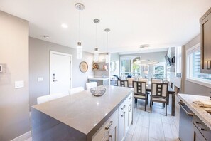 A modern kitchen with a central island, pendant lighting, and a dining area with chairs and a table.