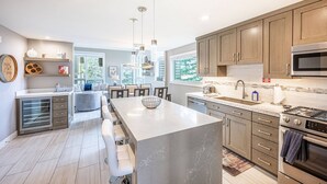A modern kitchen with a large island, wooden cabinets, stainless steel appliances, and a dining area with a view of the outdoors. - Canyons Resort Ski Home | Walk to Skiing + Free On Call Shuttle | 2 Fireplaces & 3 Cal-King Suites (Park City)