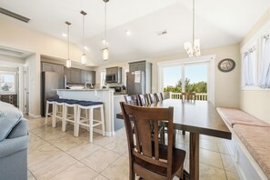 A modern kitchen with a central island, bar stools, and a dining table with chairs.