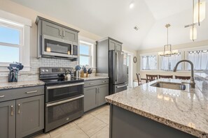 A modern kitchen with grey cabinets, stainless steel appliances, a granite countertop, and a large island with a sink.