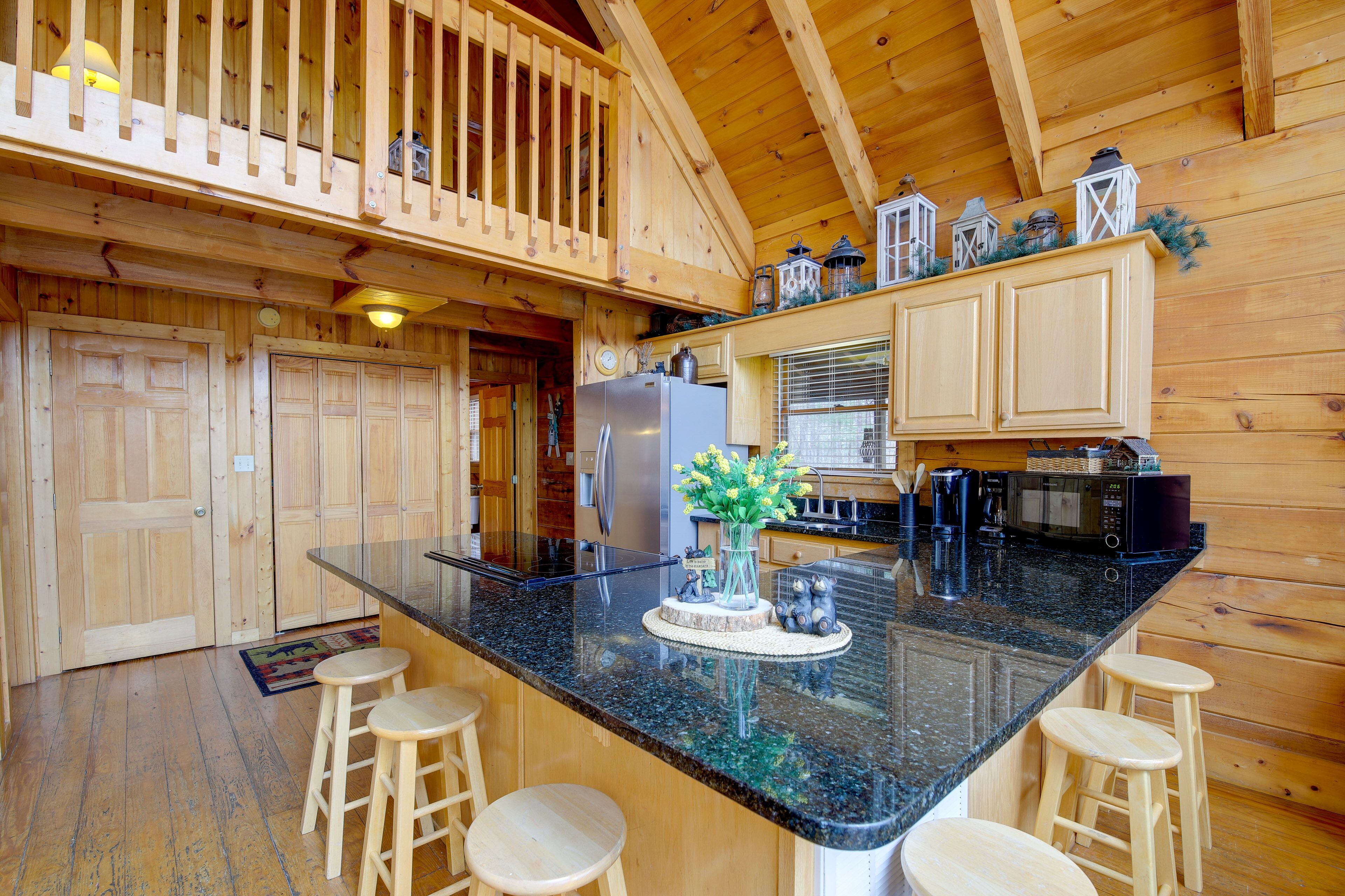 A wooden cabin interior with a kitchen featuring a granite countertop, wooden stools, and a refrigerator.