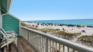 Eine Holzterrasse mit Blick auf einen Strand, Sonnenschirme und Personen.