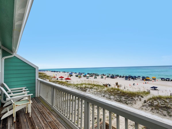 A wooden deck with a view of a beach with umbrellas and people.