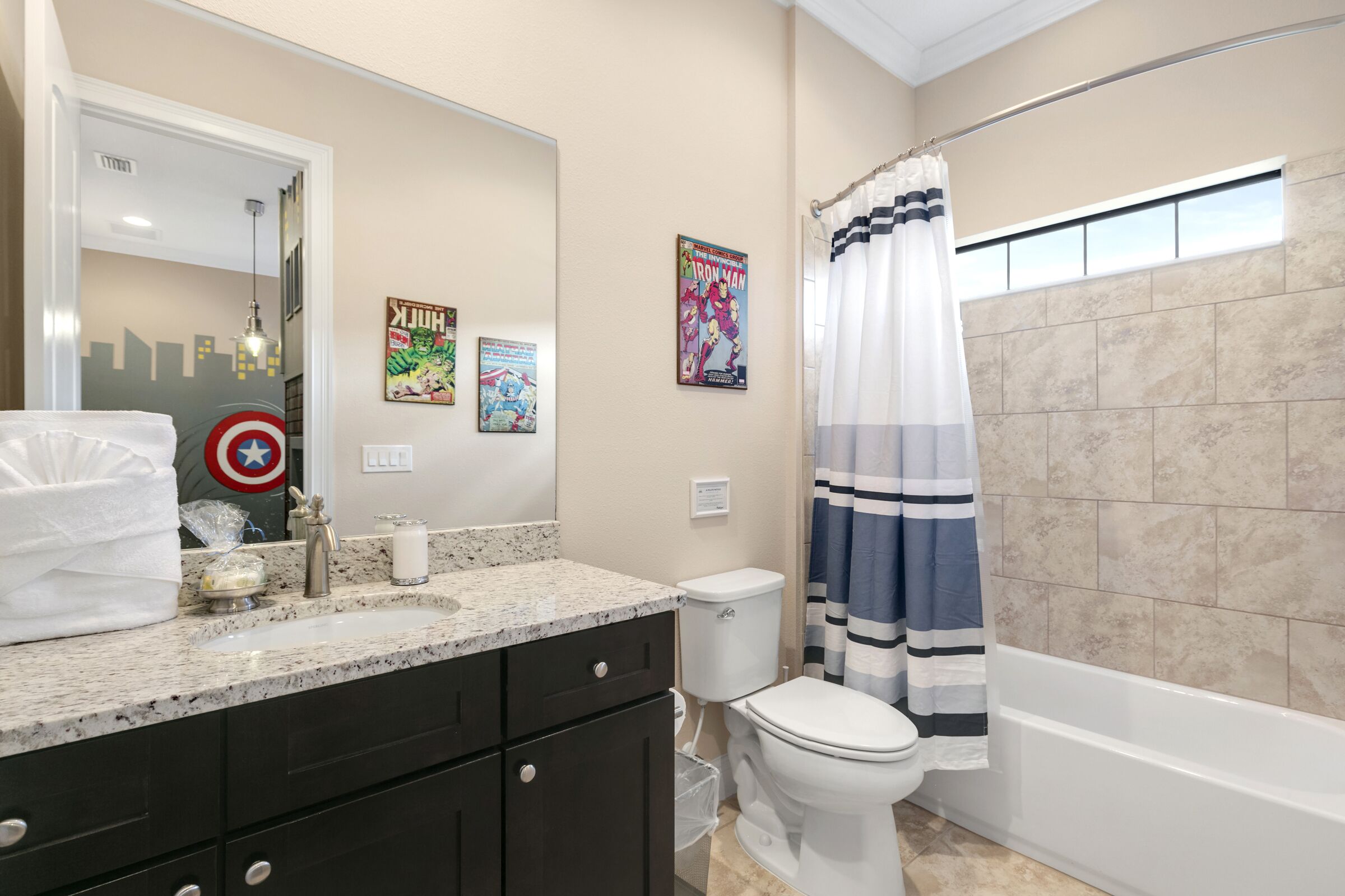 A bathroom with a sink, toilet, and bathtub. There are posters on the wall and a shower curtain.