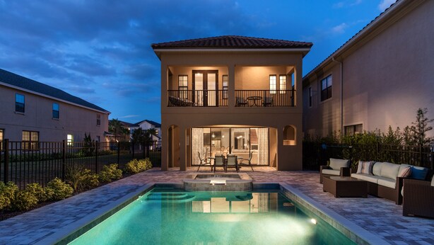 Une maison à deux étages avec une piscine, un espace salon extérieur et un balcon bien éclairé.