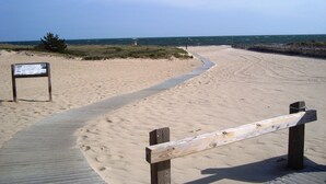 Ein Sandstrand mit einer Holzpromenade und einem Hinweisschild.