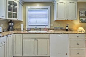 Kitchen features a central island with sink and dishwasher, ample storage in classic cabinetry, and a window with blinds.