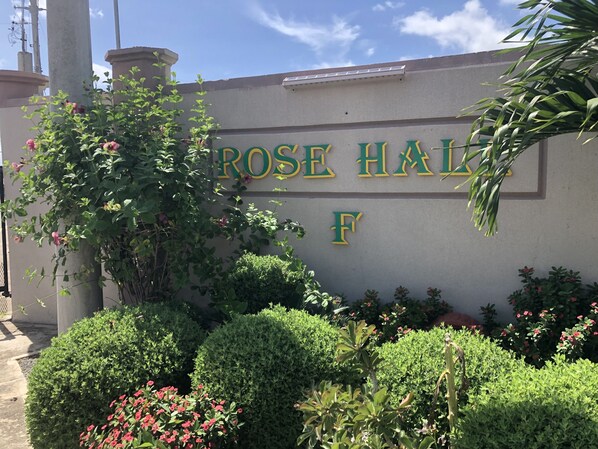 A sign for "ROSE HALL F" with surrounding greenery and a clear sky.