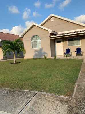 A house with a well-maintained lawn, a palm tree, and two blue chairs outside.