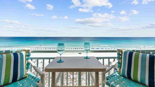 Une vue sur la plage, avec une table et des chaises, deux verres vides et un ciel dégagé.