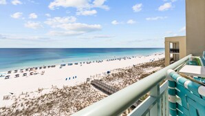 Une vue sur la plage depuis un balcon, avec un ciel dégagé, une plage de sable et quelques parasols.