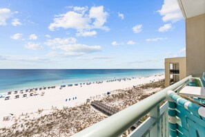 A beach view from a balcony with a clear sky, sandy beach, and a few umbrellas.