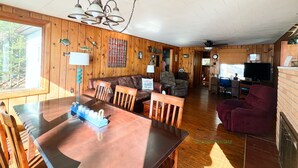 A spacious room with a wooden dining table, chairs, a sofa, and a television. - Spacious, waterfront cottage in Traverse City. Fireplace. Dog friendly. (Traverse City)