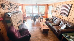 A cozy cabin interior with a wooden floor, a leather sofa, a purple armchair, and a dining area with wooden chairs and a table. - Spacious, waterfront cottage in Traverse City. Fireplace. Dog friendly. (Traverse City)