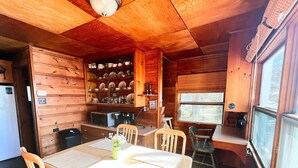 A wooden cabin interior with a dining area, kitchen, and a large window. - Spacious, waterfront cottage in Traverse City. Fireplace. Dog friendly. (Traverse City)