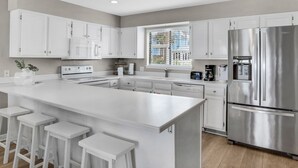 Een moderne keuken met witte kasten, een roestvrijstalen koelkast en een groot eiland met barstoelen.