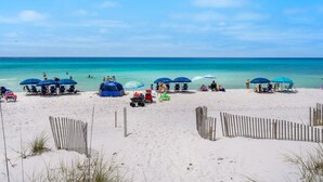 Een strand met meerdere parasols en strandstoelen, een tent en een houten omheining.