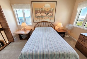 A bedroom with a bed, two bedside tables with lamps, a wall-mounted fan, and a painting of flamingos. - Dolphin Rise – Relaxation Starts Here (Topsail Beach)