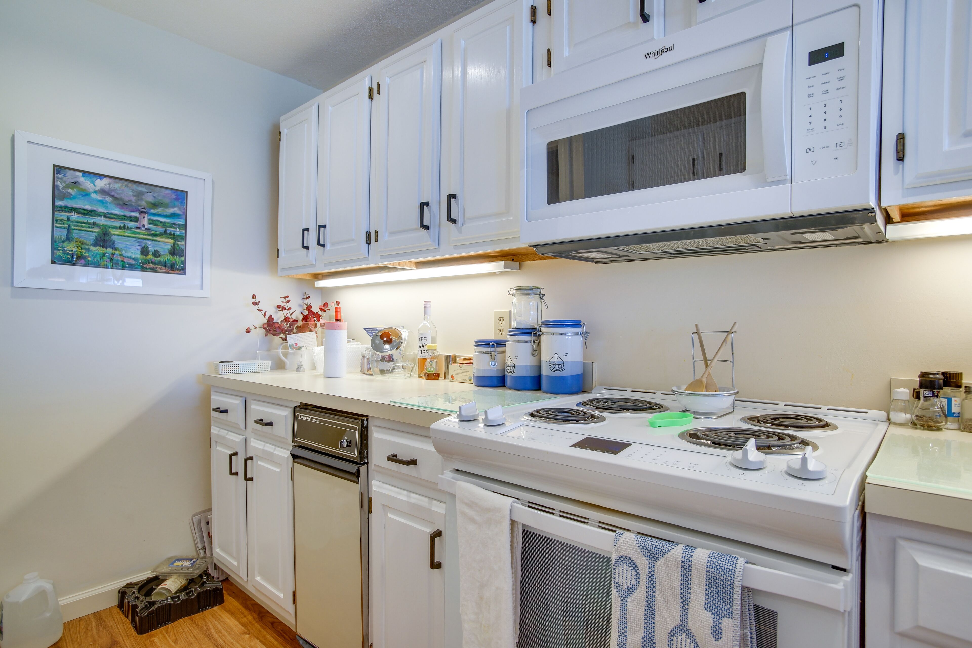 A kitchen with white cabinets, a microwave, a stove, and various kitchen items on the counter.