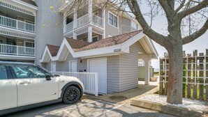 Un edificio de dos pisos con fachada blanca, un garaje y un árbol en la parte delantera.