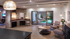 A spacious living area with a stone fireplace, a pool view through glass doors, and a cozy seating arrangement.