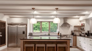 A modern kitchen with a large island, stainless steel appliances, and a view of greenery through the windows.