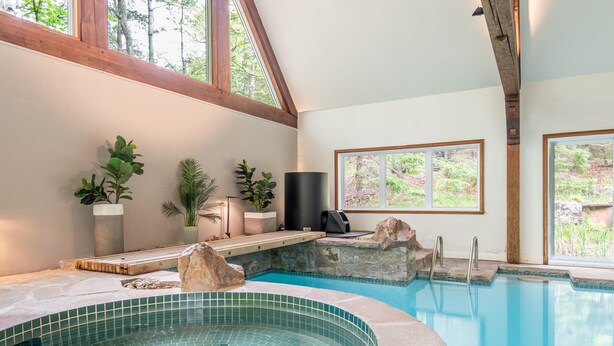 A swimming pool with a tiled edge, wooden beams, and potted plants.