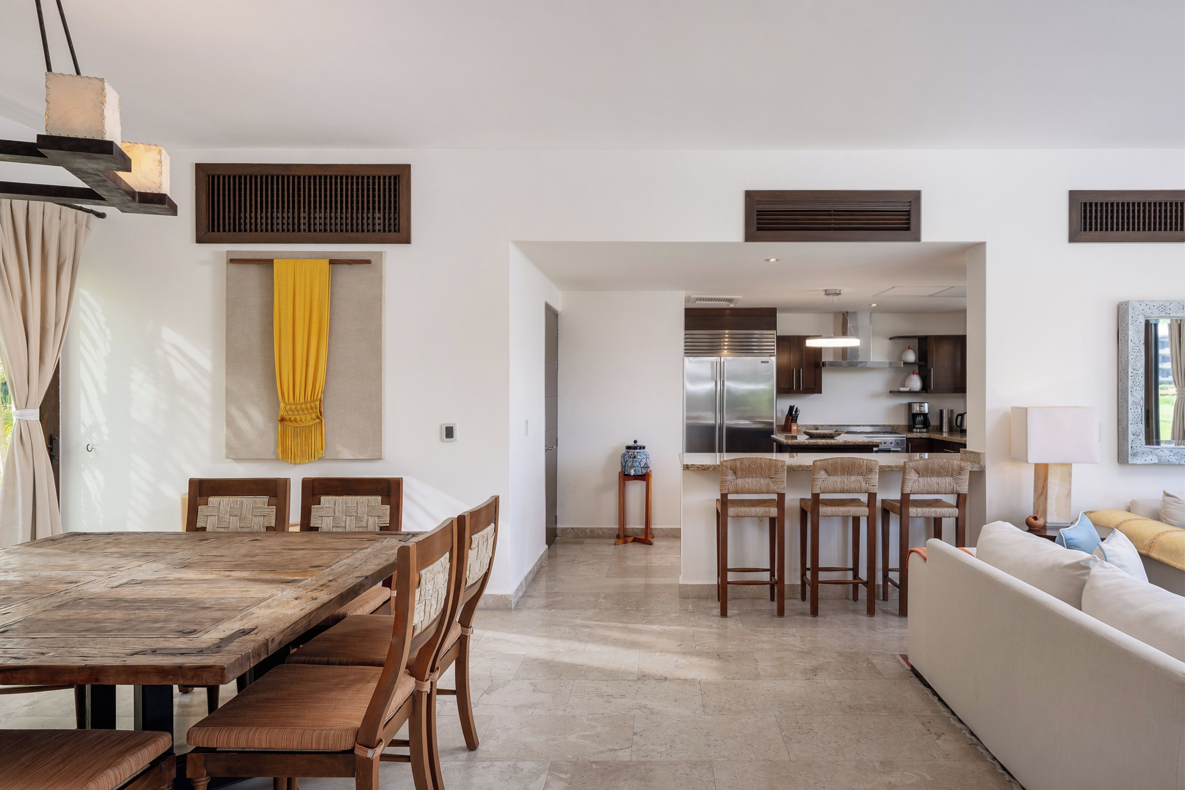 Cozinha moderna com eletrodomésticos de aço inoxidável, sala de jantar com mesa e cadeiras de madeira e sala de estar com sofá e mesa de centro.