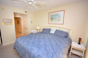 A bedroom with a large bed, a ceiling fan, a nightstand, a lamp, and a framed picture on the wall. - Bright, cozy luxury 3 bedroom ocean block condo with WiFi and an outdoor pool located near downtown and less than a block from the beach! Linens included and beds maid, hotel service in the condo. (Ocean City)