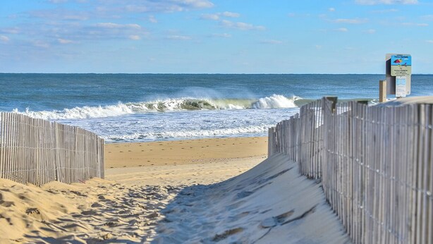 Una spiaggia con una recinzione di legno che conduce verso l'oceano, un cartello e una battigia sabbiosa.