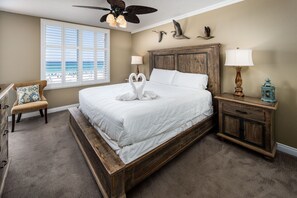 Quarto com uma cama grande, uma cadeira, mesa de cabeceira e janela com vista para a praia.