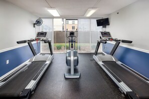Ein Fitnessraum mit Laufbändern, Crosstrainern und einem Ventilator.