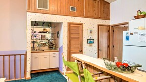 Een kleine keuken met houten kastjes, een wit aanrecht en een groene stoel.
